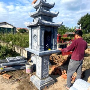 Cây hương đá xanh ba tầng mái đặt trên trụ chạm hoa văn, thợ đang lắp đặt