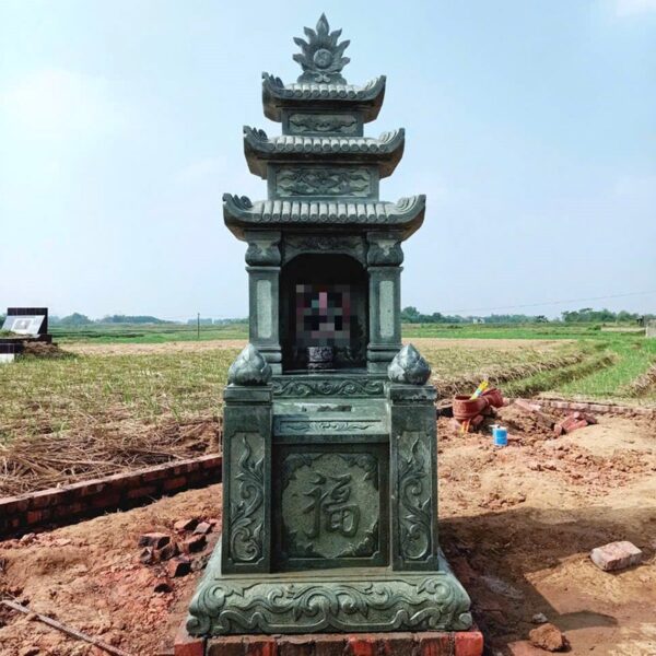 Mộ ba mái đá xanh rêu, thân mộ chạm chữ Phúc, đặt giữa cánh đồng