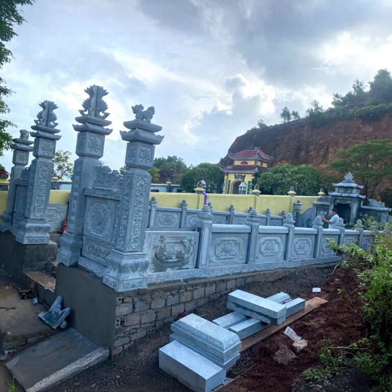 Tường rào và trụ cổng đá xanh chạm hoa văn bao quanh khu lăng trên sườn đồi
